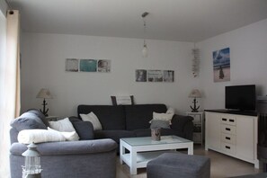 A living room with a sofa, a coffee table, a TV, and artwork on the wall. - Thatched holiday home with sauna (Koserow)