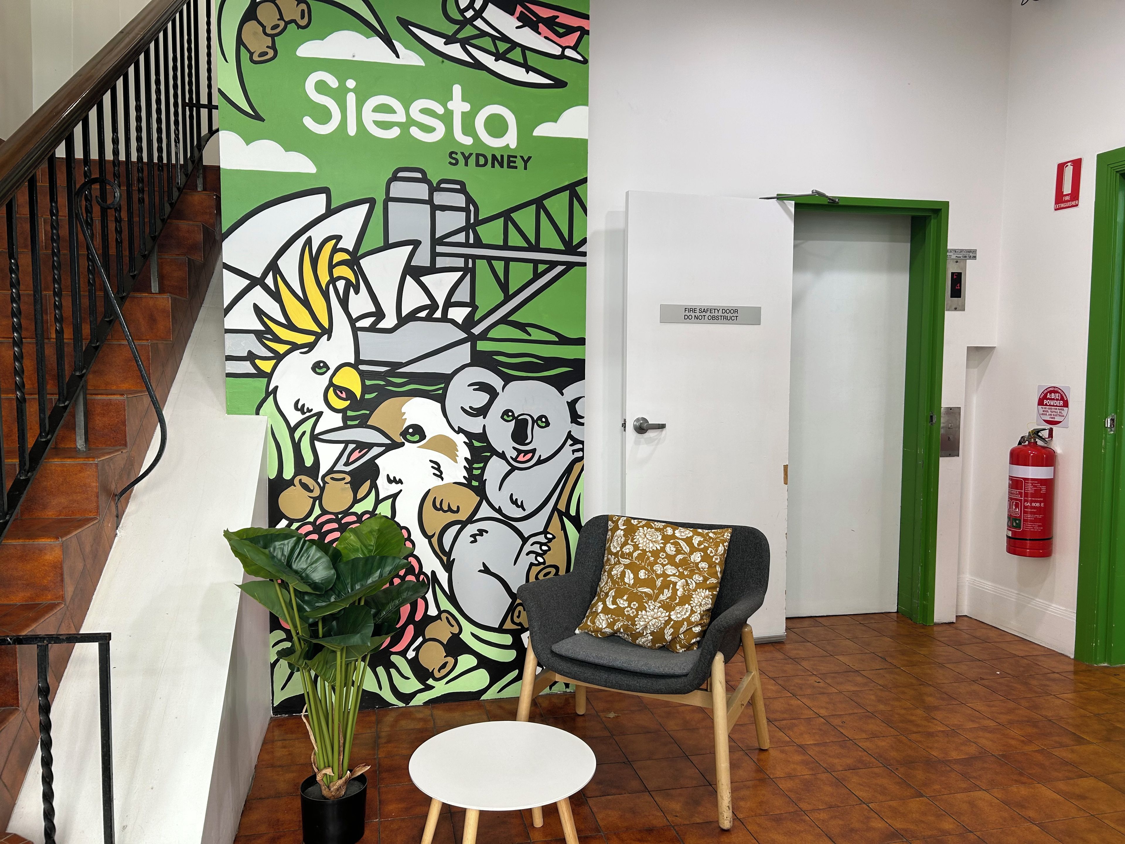 A lobby with a mural, a staircase, a chair, a table, and a fire extinguisher.