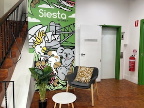A lobby with a mural, a staircase, a chair, a table, and a fire extinguisher. - Siesta Sydney (Sydney)