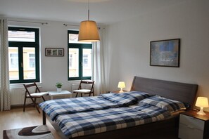 A bedroom with a bed, bedside tables, a desk, chairs, and a window with curtains. - Trade Fair Apartment Lindenau (Leipzig)