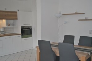 A modern kitchen with white cabinets, a built-in oven, and a dining area with a table and chairs. - Trade Fair Apartment Lindenau (Leipzig)