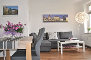 A modern living room with a sofa, a coffee table, and a dining table with a vase of flowers. - Trade Fair Apartment Lindenau (Leipzig)