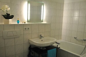 A bathroom with a white sink, a mirror, a bathtub, and a towel rack. - Trade Fair Apartment Lindenau (Leipzig)
