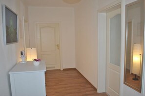 Ein Flur mit einer weißen Tür, einem kleinen weißen Schrank mit einer Vase und einem Spiegel, der eine Lampe reflektiert.