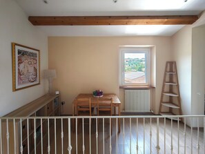 Ein Zimmer mit Holzboden, einem Fenster mit Aussicht, einem Heizkörper, einem Tisch mit Stühlen und einer Leitern.