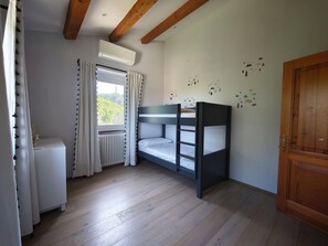 Ein Zimmer mit Etagenbett, Heizkörper, einem Fenster mit Vorhängen und einer Holztür.