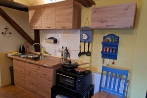 Een compacte keuken met houten kastjes, een inbouwoven en een klein eethoekje met een blauwe stoel.