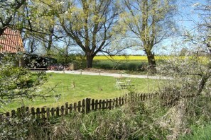 A rural landscape with a large tree, a wooden fence, and a building with a tiled roof. - Holiday home with 1 bedroom (Neuharlingersiel)