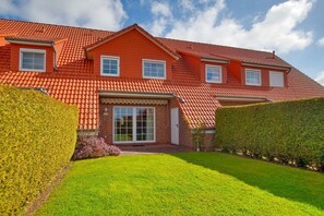 A two-story house with a red-tiled roof, a front entrance with glass doors, and a well-maintained lawn. - Schneider Hengsthamm 5b (Hooksiel)