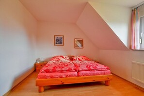 A bedroom with a sloped ceiling, a wooden bed, two framed pictures on the wall, and a window with curtains. - Schneider Hengsthamm 5b (Hooksiel)