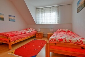 A bedroom with two single beds, a window with sheer curtains, a radiator, and a red rug. - Schneider Hengsthamm 5b (Hooksiel)