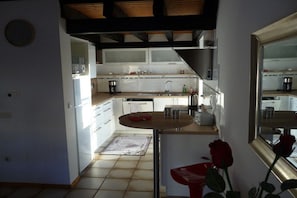 A kitchen with white cabinets, a sink, and a dining area with a table and chairs. - Holiday home with 2 bedrooms (Birkenhördt)