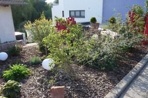 A garden with various plants and a white building in the background. - Holiday home with 2 bedrooms (Birkenhördt)