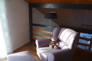 A room with a wooden ceiling, a purple armchair, a white sofa, and a floor lamp. - Holiday home with 2 bedrooms (Birkenhördt)
