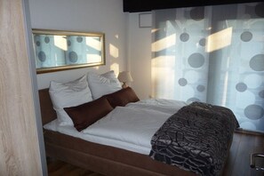 Een net opgemaakt bed met een bruin hoofdbord, een bedlampje en een raam met ronde patronen.