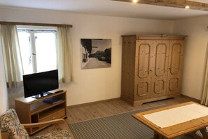Ein Wohnzimmer mit Fernseher auf einem Holzboden, einem Schrank, einer Couch und einem Teppich.