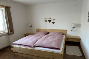 A single bed with a wooden frame and a headboard, two bedside tables, a window with curtains, and a wall-mounted light fixture. - Holiday apartment with 2 bedrooms (Mittenwald)