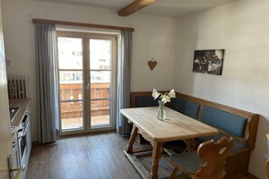 A room with a wooden table, bench seating, a radiator, and a window with curtains. - Holiday apartment with 2 bedrooms (Mittenwald)