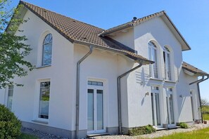 Ein zweistöckiges Haus mit Satteldach, weißen Außenwänden und mehreren Fenstern.