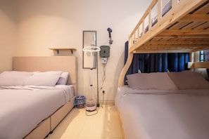 Et lille værelse med to senge, en fastgjort varmeblæser og en ventilator i loftet.