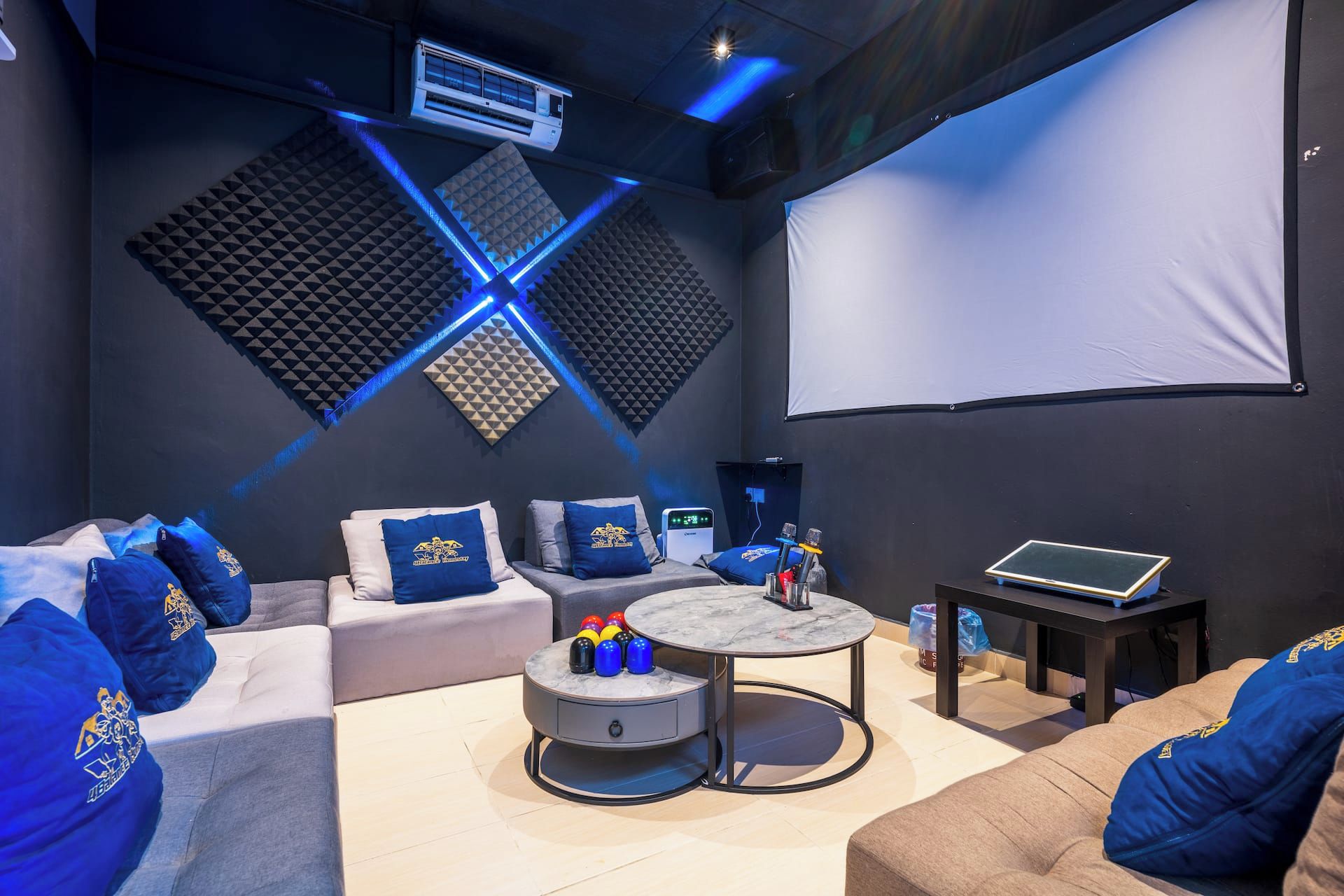 Un espacio lounge moderno con pantalla de proyector, asientos cómodos, una pequeña mesa y un equipo de sonido.