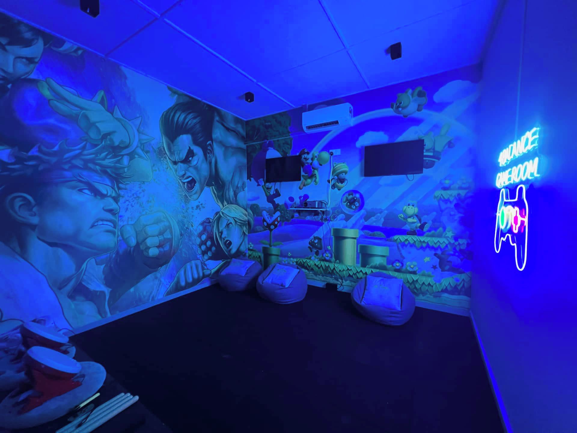Una habitación con un mural, pufs, un letrero de neón y un televisor de pantalla plana.