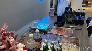 A room with a neon sign, a table with food items, drinks, and utensils.