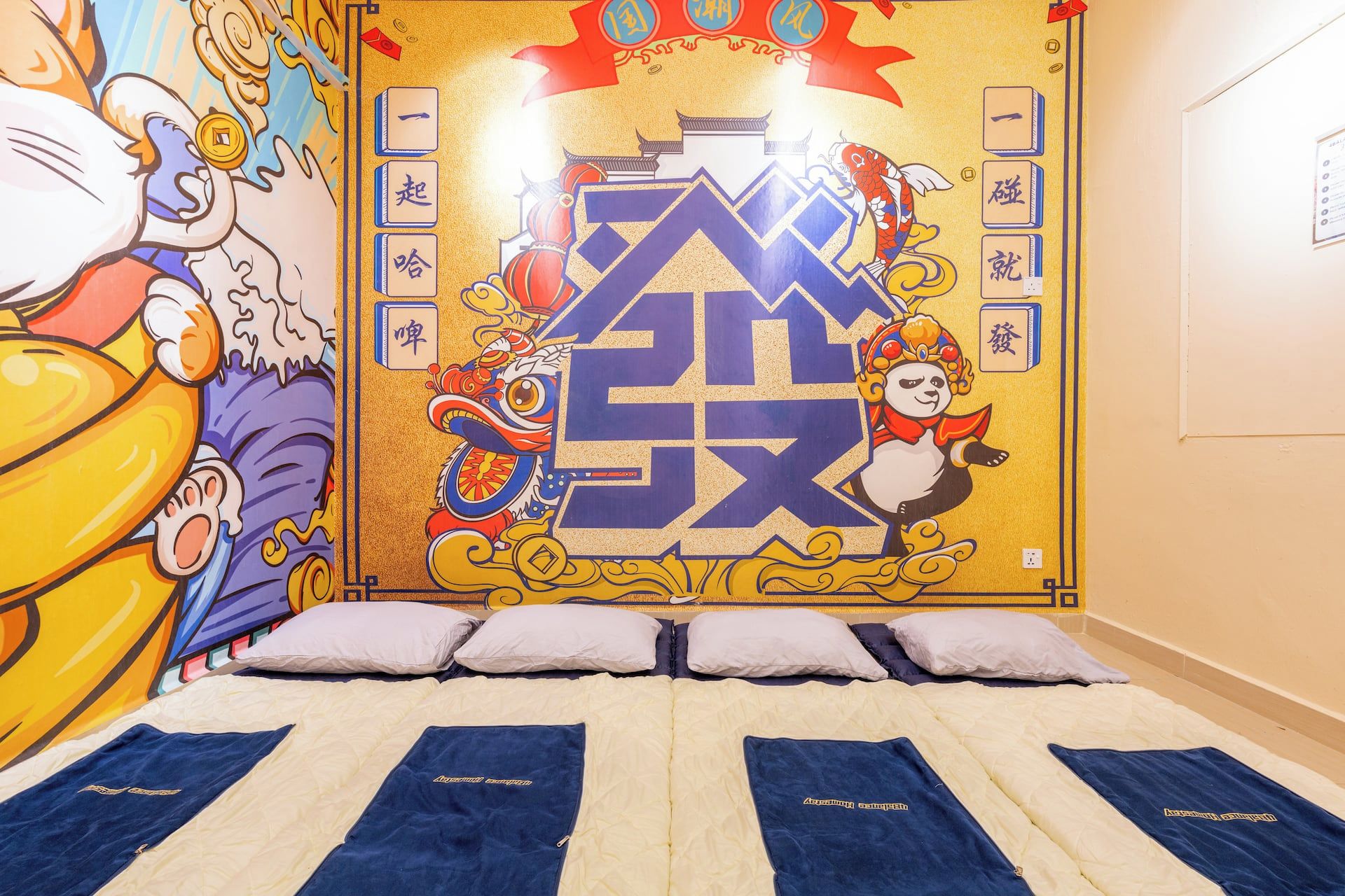 Una habitación con un mural grande, una cama con ropa de cama azul y blanca, y un televisor montado en la pared.