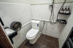 Et lille badeværelse med toilet, bruser og et hylder med toiletartikler.