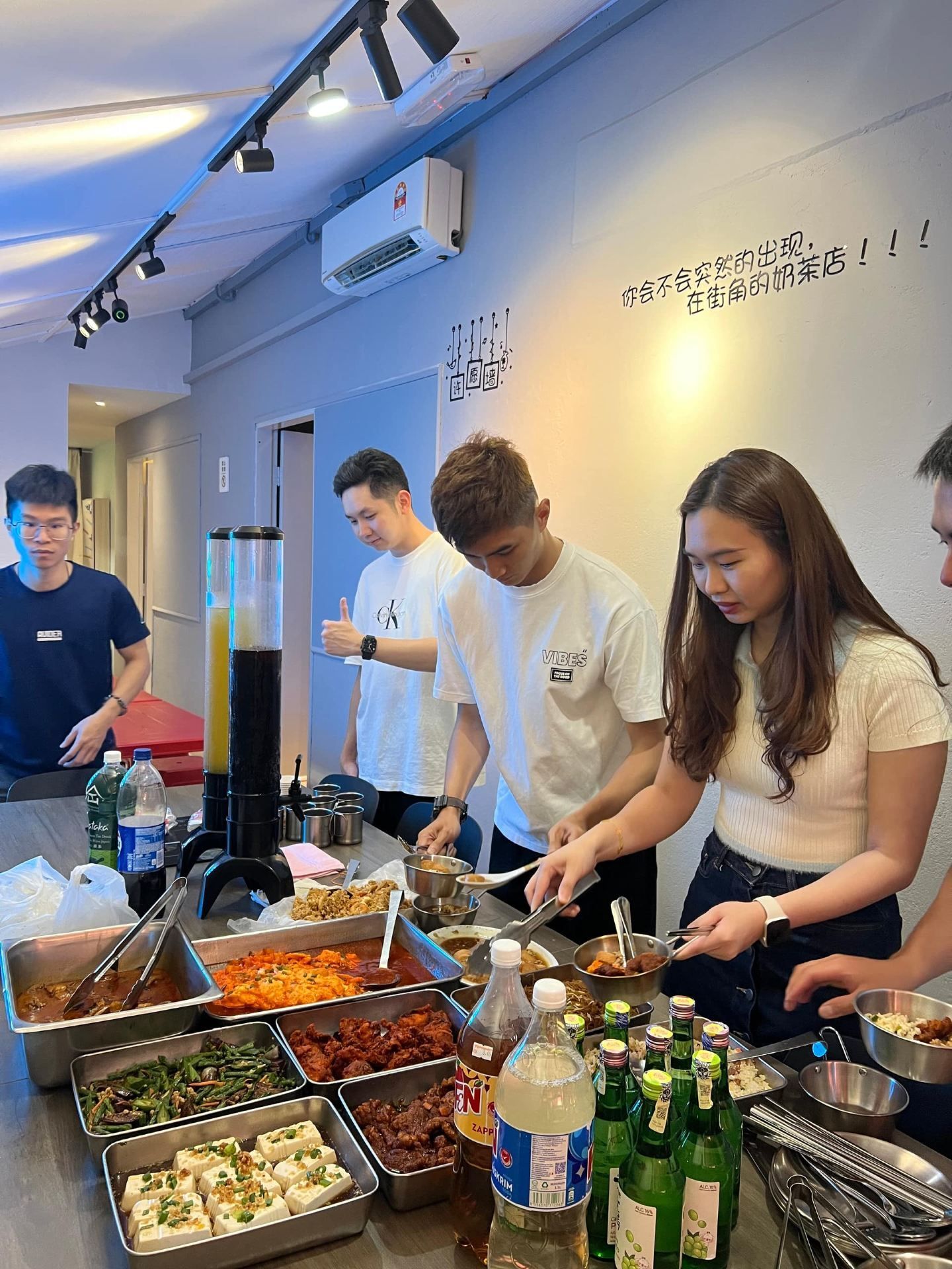 A group of people serving themselves from a buffet with various dishes and beverages.