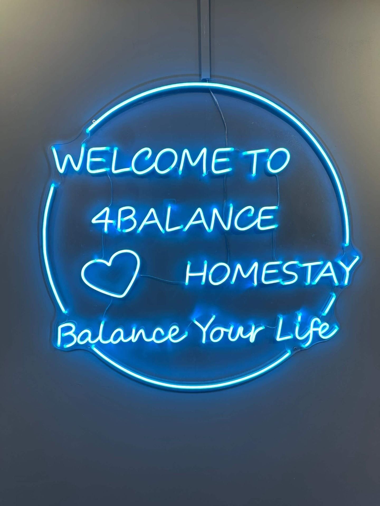 A neon sign with the text 'WELCOME TO 4BALANCE HOMESTAY Balance Your Life'.