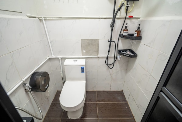 Une petite salle de bain compacte, équipée de toilettes, d’une douche et d’un sèche-mains.
