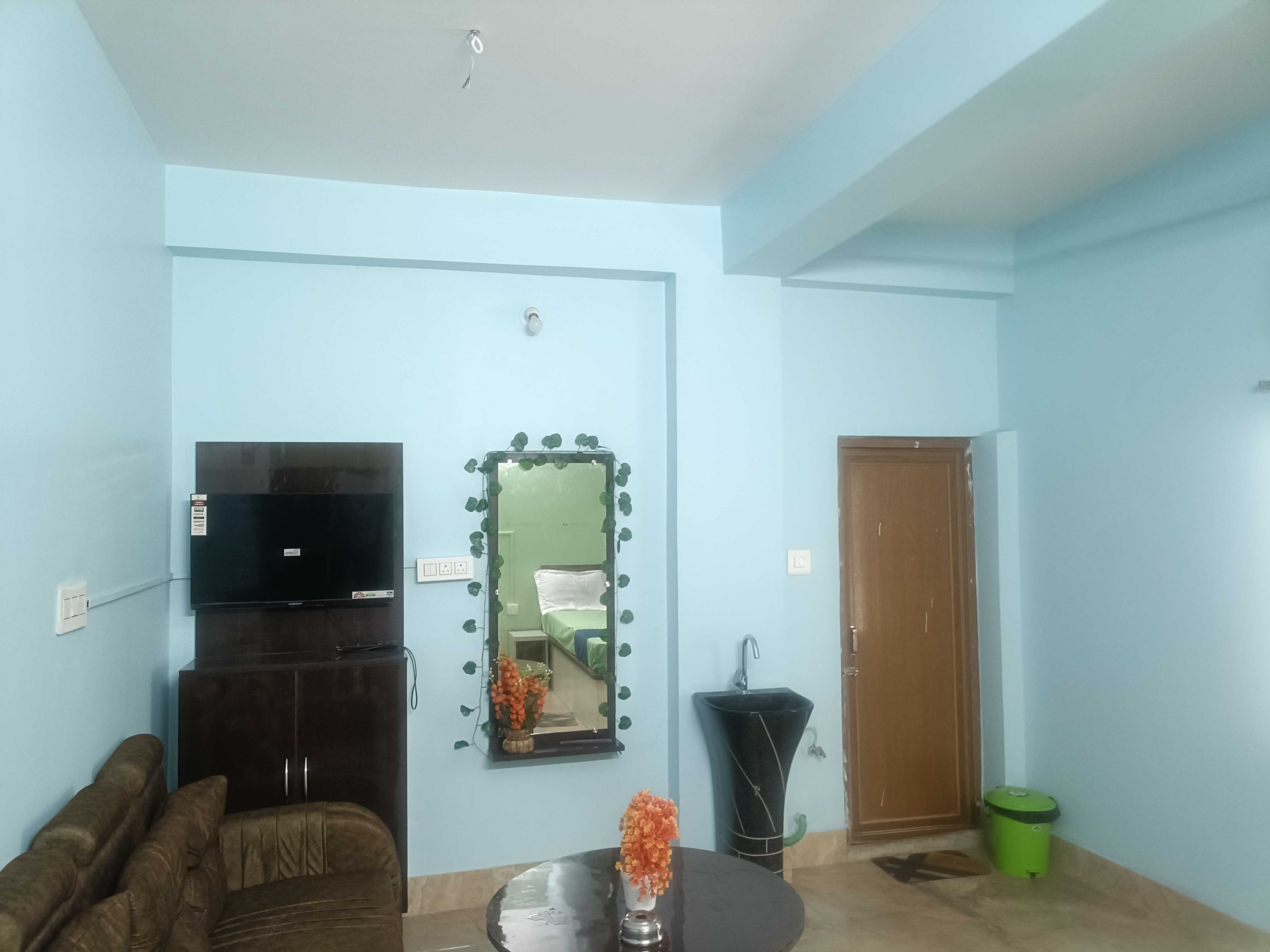 Una sala de estar con televisor, sofá, una mesa con un florero, un espejo y una puerta.