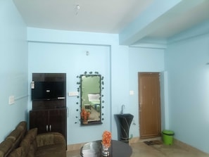Una sala de estar con televisor, sofá, una mesa con un florero, un espejo y una puerta.