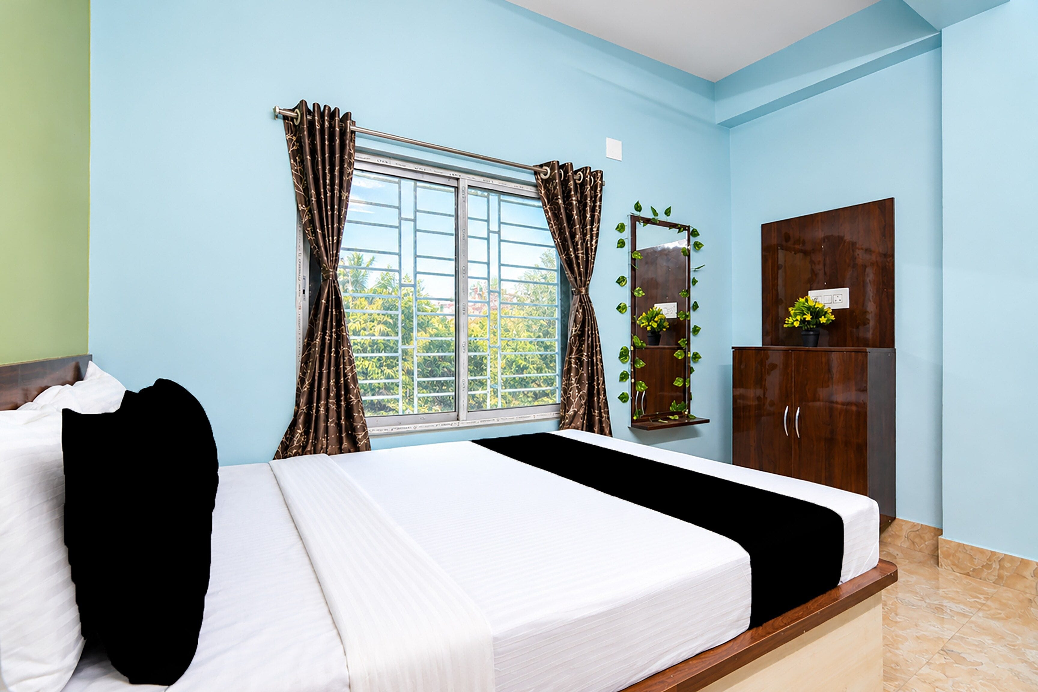 A bedroom with a bed, a window with curtains, a mirror, and a wardrobe.