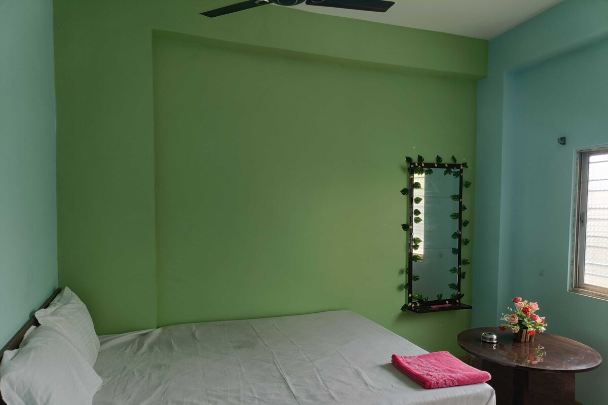 A room with a bed, a small table with a vase of flowers, a mirror, and a window.