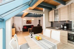 Eine moderne Küche mit Holzausstattung, einem Esstisch mit Obstschale und einer gemütlichen Wohnbereich mit Sofa und Kamin.