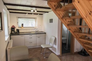 Eine Küche mit Spüle, Schränken und einem Stuhl. Ein Fenster mit Jalousien und ein Bild an der Wand sind ebenfalls vorhanden.