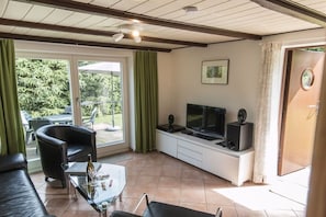 Ein Wohnzimmer mit einer Couch, einem Couchtisch, einem Fernseher und einer Schiebetür zum Garten.