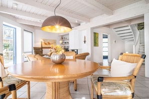 A dining area with a round wooden table, wicker chairs, and a hanging pendant light. - Up to 6 holidaymakers (Ostseeheilbad Zingst)