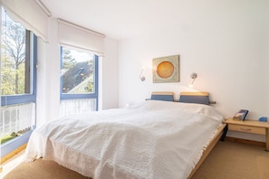 A bedroom with a large bed, a nightstand, a wall-mounted lamp, and a window with a view of the outside. - Up to 6 holidaymakers (Ostseeheilbad Zingst)
