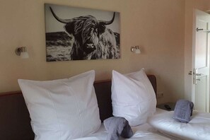 A hotel room with two beds, white bedding, a wall-mounted artwork of a bull, and a door to the right. - Holiday home with 1 bedroom (Reit im Winkl)