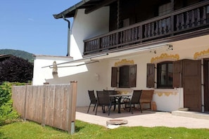 A two-story building with a balcony, a dining area with chairs and a table, and a wooden fence. - Holiday home with 1 bedroom (Reit im Winkl)