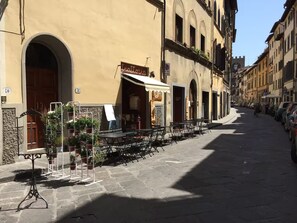 A street with outdoor seating, a building with a sign reading 'trattoria,' and parked cars along the sidewalk. - New Listing (Firenze)