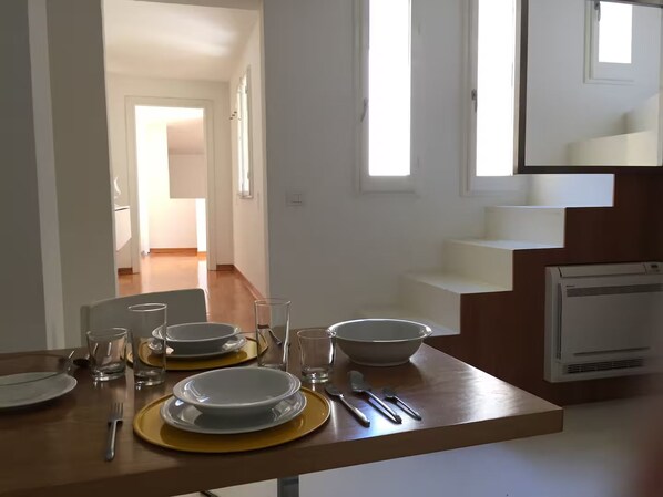 A dining area with a table set for four, a kitchen area with a stove, and a staircase leading to an upper level. - New Listing (Firenze)