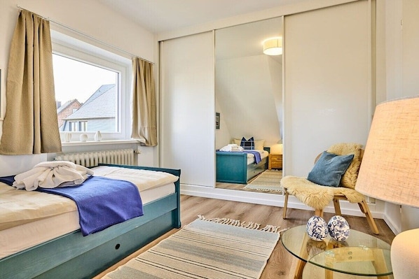 A bedroom with a bed, a mirror, a chair, and a table. - Holiday home with 3 bedrooms (Wenningstedt)