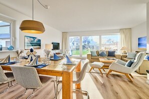 A modern living room with a wooden dining table set for four, a sofa, and a coffee table. - Holiday home with 3 bedrooms (Wenningstedt)