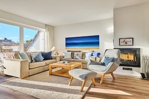 A living room with a sofa set, a coffee table, a fireplace, and a large window with a view of a building. - Holiday home with 3 bedrooms (Wenningstedt)
