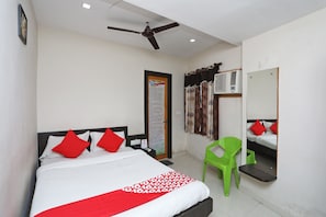A hotel room with a bed, a ceiling fan, an air conditioning unit, a green chair, and a mirror on the wall. - Hotel O South Inn (Kolkata)