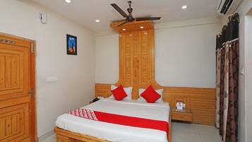 A hotel room with a wooden bed, a ceiling fan, an air conditioning unit, and a single bedside table.